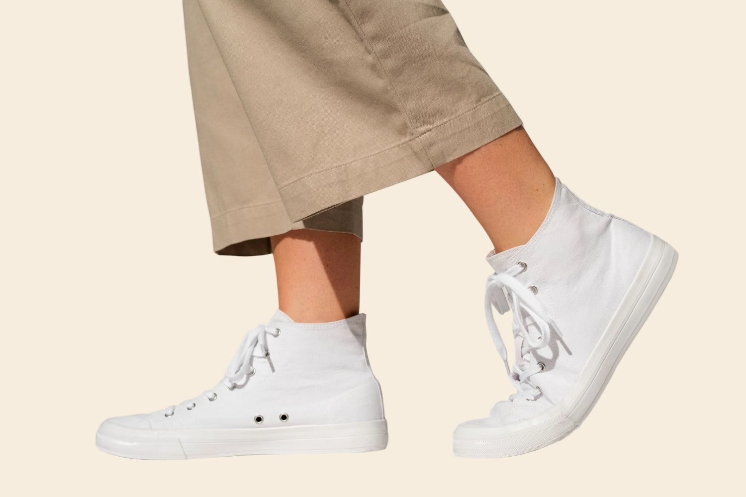 White high-top sneakers worn with beige pants on a neutral background
